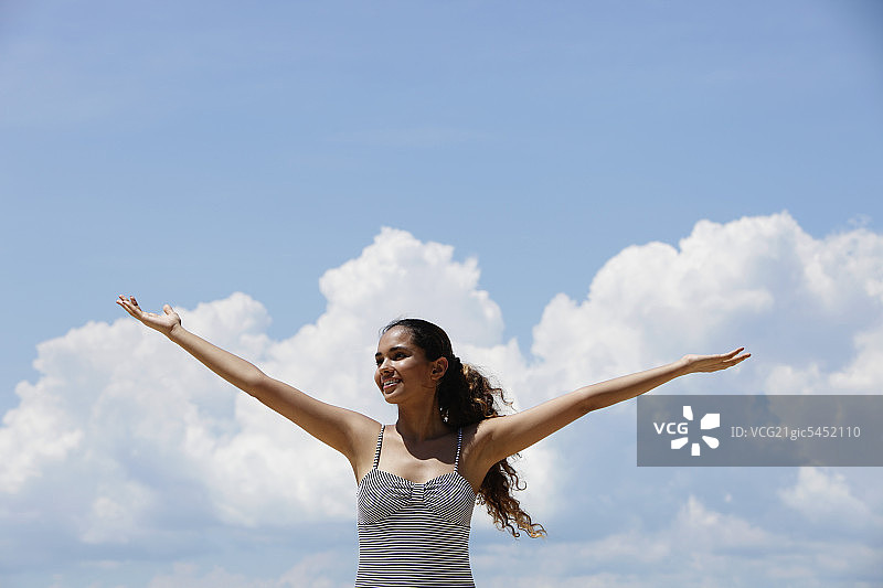 年轻女子在蓝天白云的背景下举起双臂图片素材