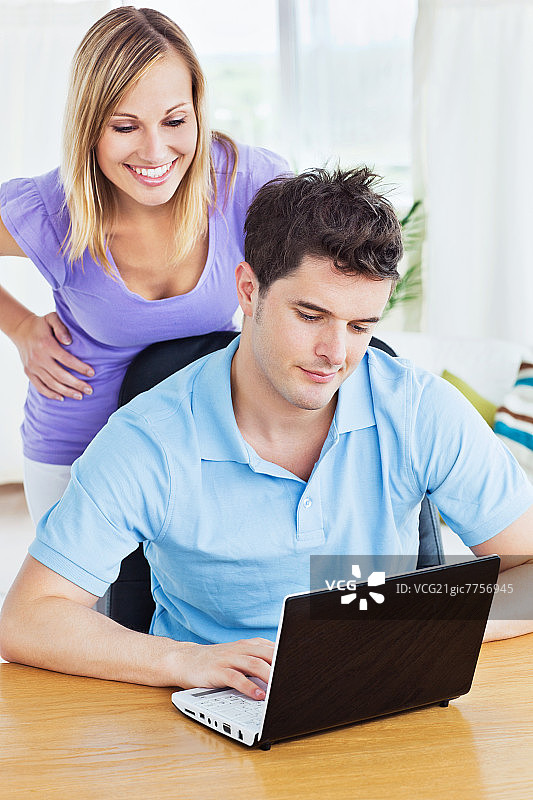 一个正经男人在用笔记本电脑，女朋友在后面看他在家工作图片素材