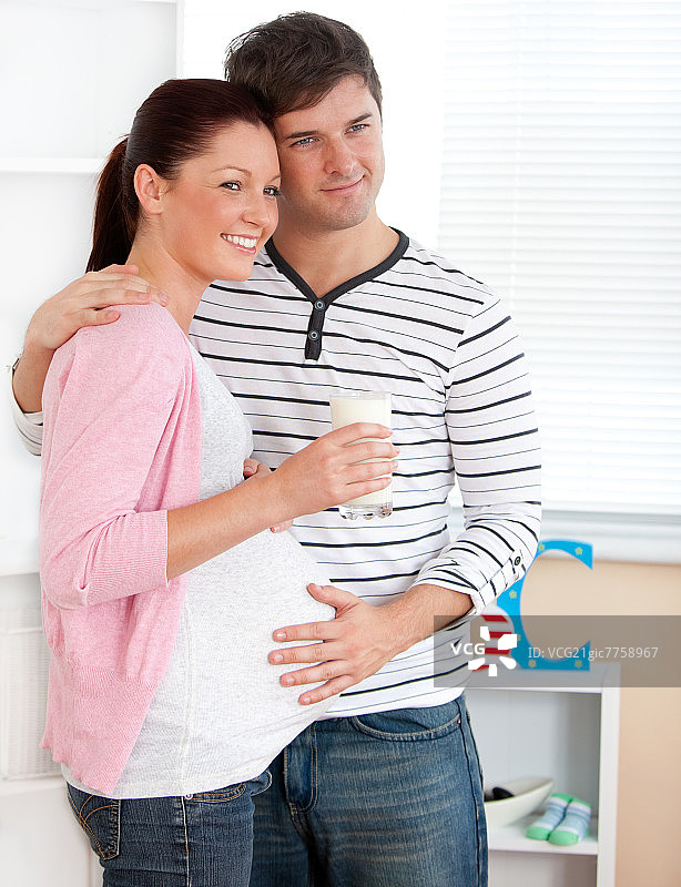 一个微笑的孕妇拿着一杯牛奶和她的丈夫在家里的肖像图片素材