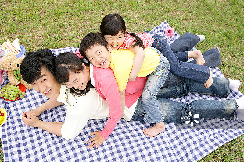 父母和孩子(6-7)躺在野餐毯子上，面带微笑，俯瞰高处图片素材