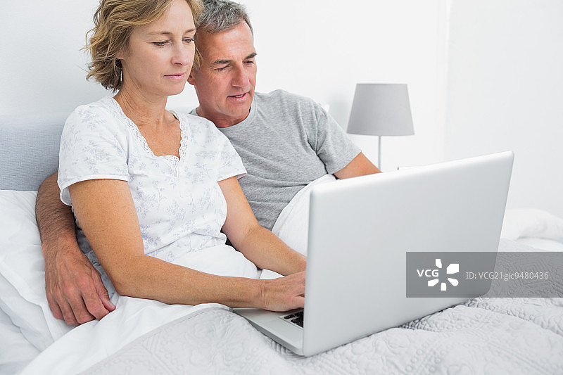 一对幸福的夫妇在卧室的床上一起使用他们的笔记本电脑图片素材