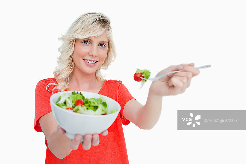 一个年轻的金发女人在白色的背景下端着一碗新鲜的沙拉图片素材