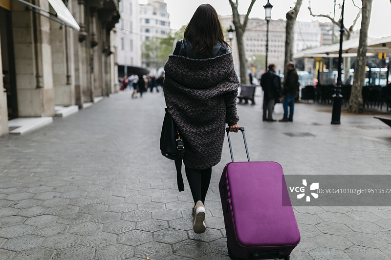 西班牙，巴塞罗那，年轻女子提着行李箱走在城市里图片素材