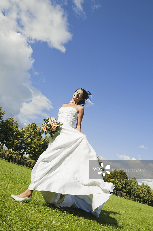 德国，巴伐利亚，新娘在公园里跑步，手持一束鲜花，微笑着，低角度观看图片素材