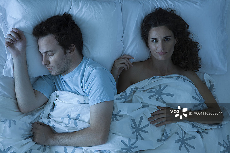 一对夫妇躺在床上，女人醒着，目光转向别处沉思图片素材