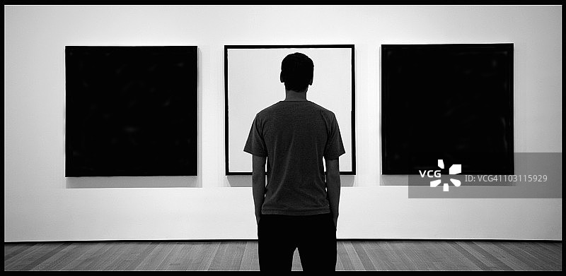 一个年轻人在博物馆里观看镶框的图像。图片素材