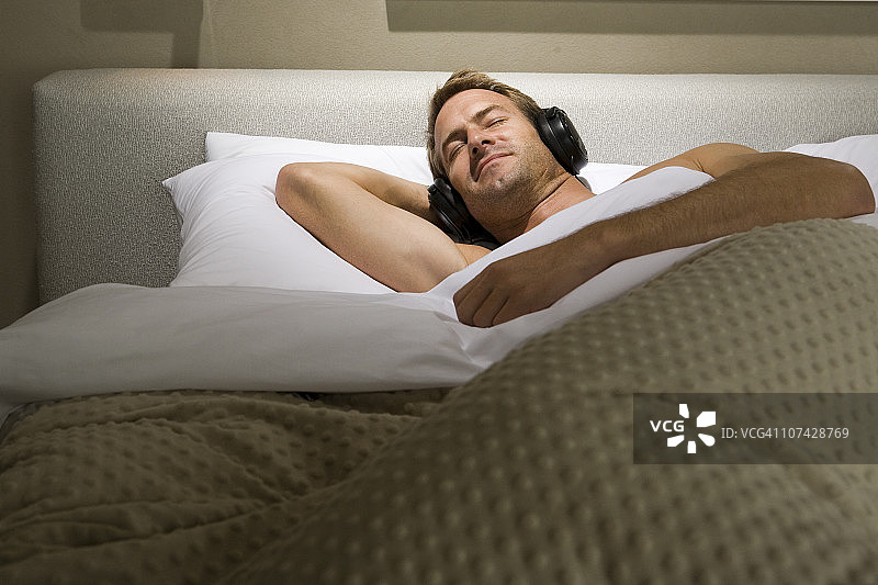 戴着耳机睡在床上的男人图片素材