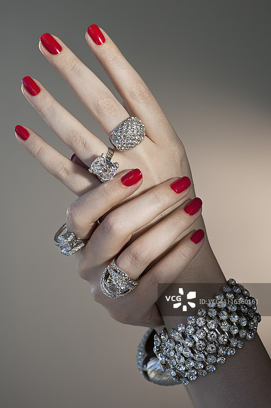 近距离的女人的手与红色指甲油和钻石珠宝图片素材