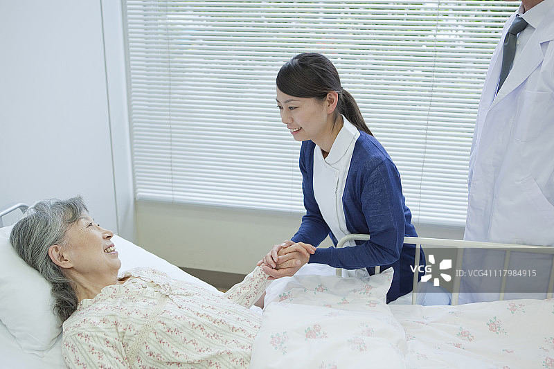 日本本州神奈川县，一位老年妇女躺在床上与护士和医生交谈图片素材