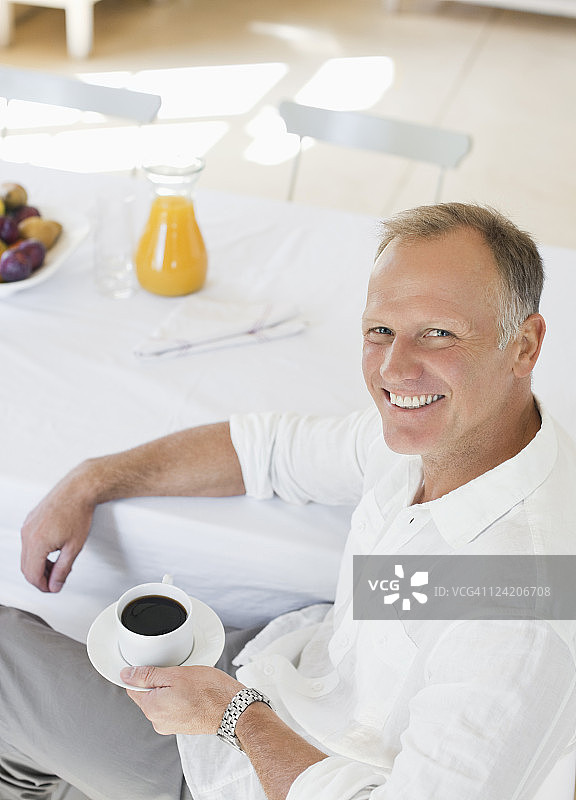 微笑的成熟男人在早餐桌上喝着咖啡图片素材