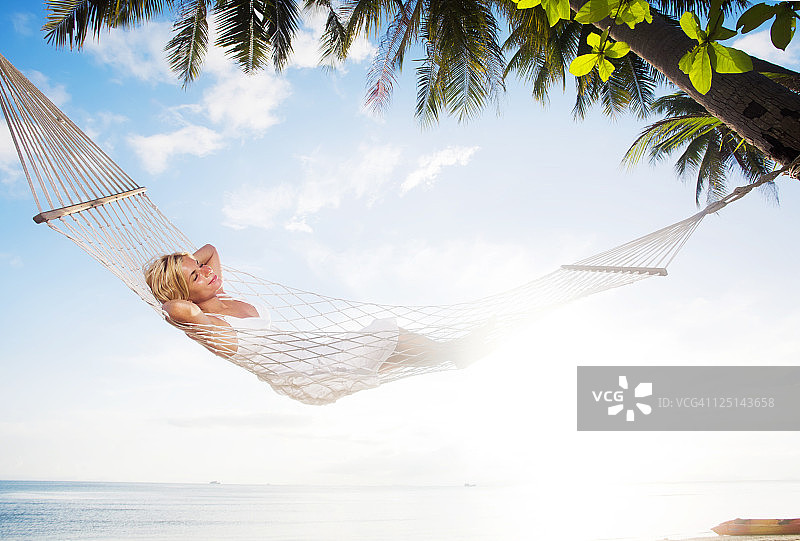 一名年轻女子在热带海滩的吊床上休息。图片素材