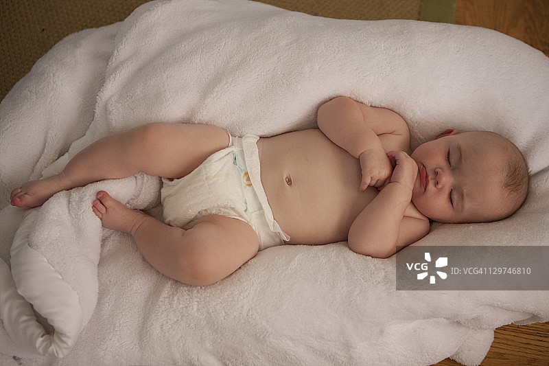 睡在白色毯子上，裹着尿布的女婴。图片素材