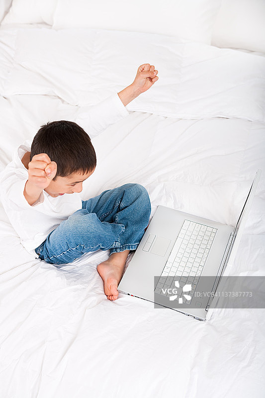兴奋的男孩在床上使用笔记本电脑图片素材