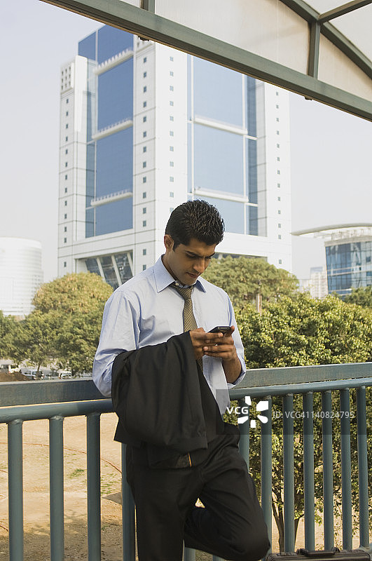 印度哈里亚纳邦古尔加翁，一名商人站在人行桥上用手机发短信图片素材