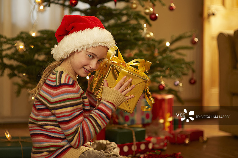 女孩把圣诞礼物举到耳边。图片素材