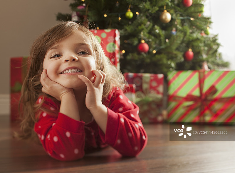 一个白人女孩躺在圣诞树旁的地板上图片素材