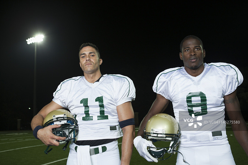 橄榄球运动员肩并肩站着，拿着头盔图片素材