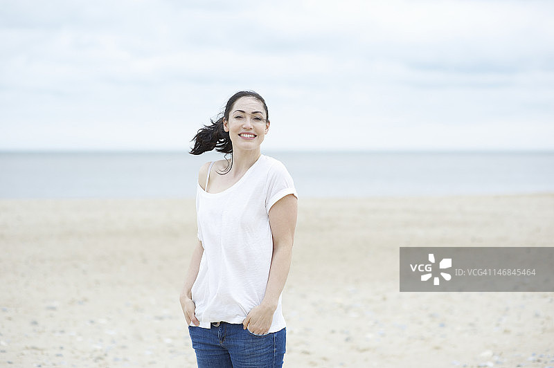 站在沙滩上微笑的女人。图片素材