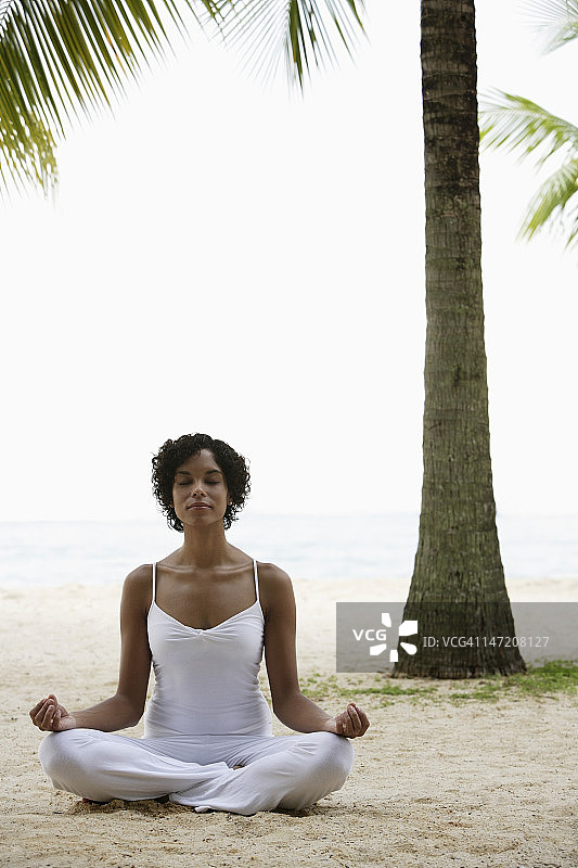 坐在海滩上做瑜伽的女人，闭着眼睛。图片素材