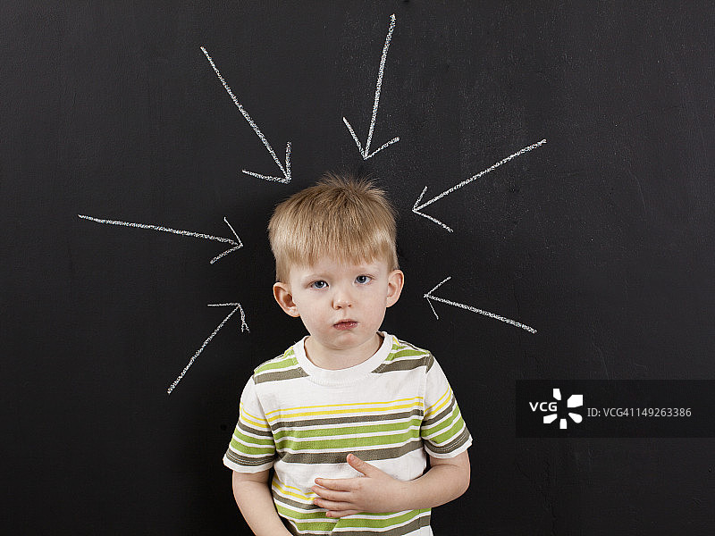 可爱的蹒跚学步的男孩(2-3)站在黑板上，用粉笔写的箭头指向他图片素材
