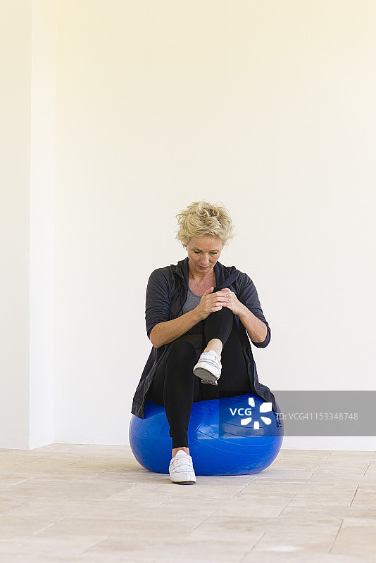 成熟的女人坐在健身球上，抱着单膝图片素材