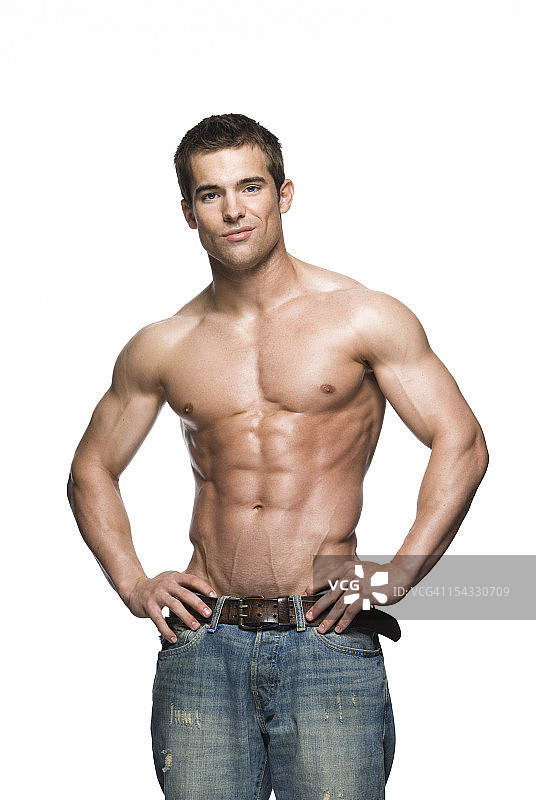 年轻肌肉男穿着牛仔裤，双手叉腰，在摄影棚拍摄图片素材