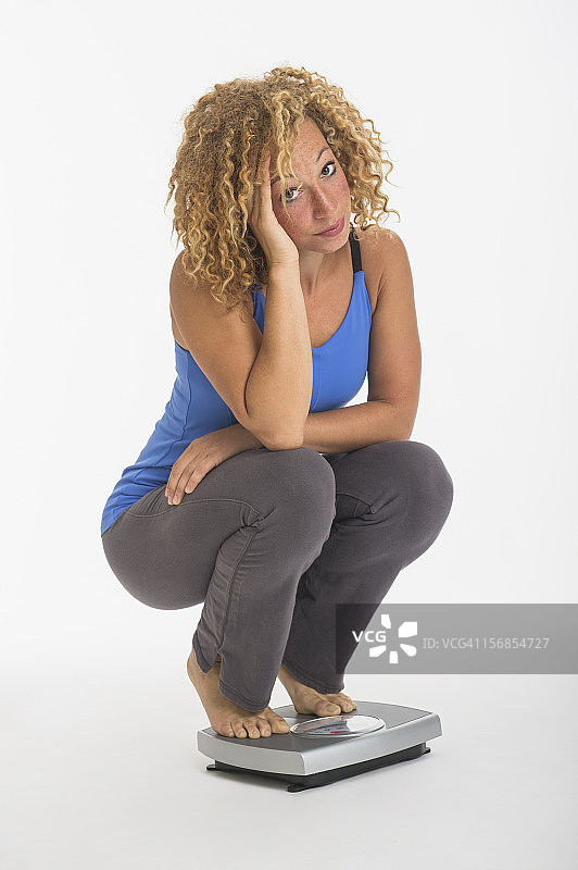 一名年轻女子蹲在体重秤上的肖像，摄影棚里拍摄图片素材