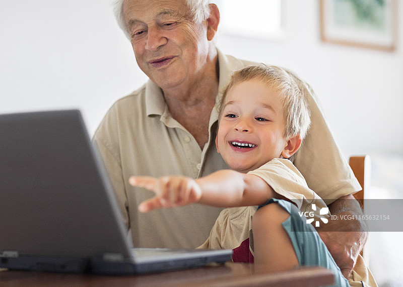 爷爷和小孙子看着笔记本电脑，一起笑图片素材