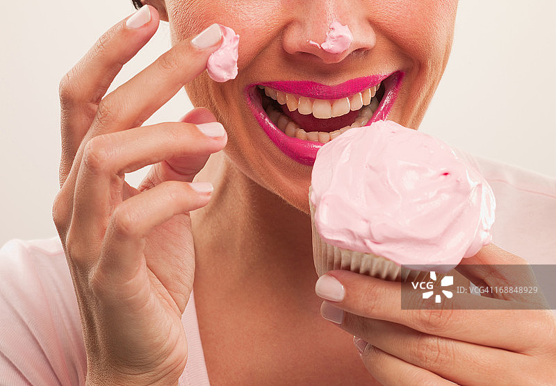 涂着粉色口红，鼻子上沾着糖霜的女人在吃纸杯蛋糕图片素材