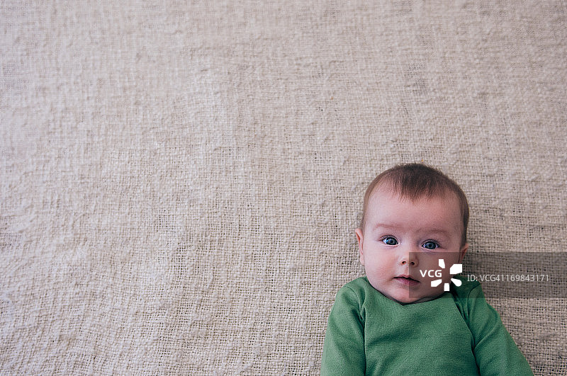 婴儿(3-6个月)躺在地板上。绿色的衬衫。俯视图图片素材