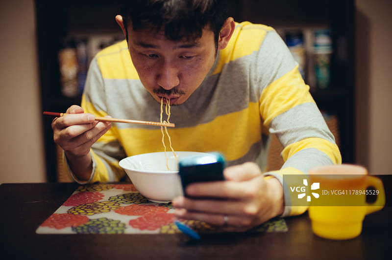 一名日本男子一边吃面条一边看书图片素材
