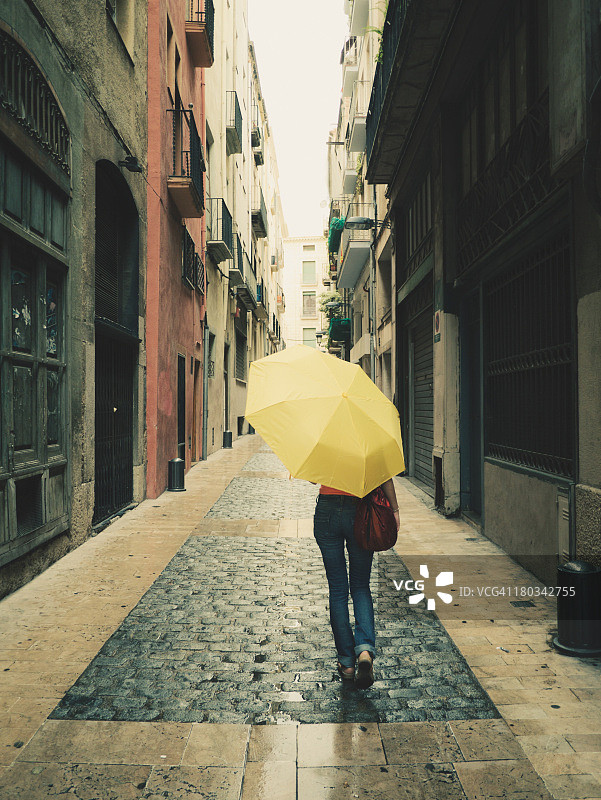 带着黄色雨伞在雨中行走的女孩图片素材