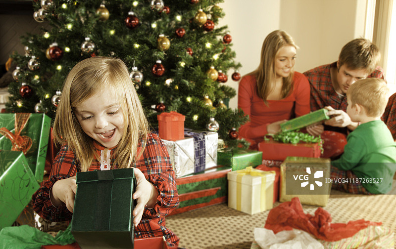 小女孩在圣诞节早上打开礼物，家人在后面图片素材