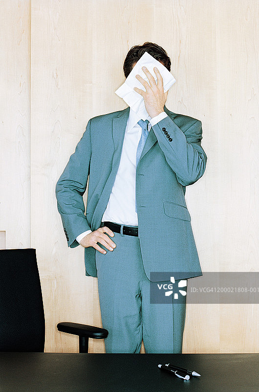 一个商人站在桌子后面，拿纸巾贴着脸图片素材