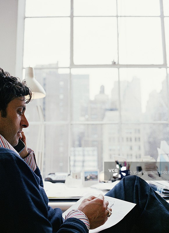 一个人在桌边用电话，靠近窗户，侧面图片素材