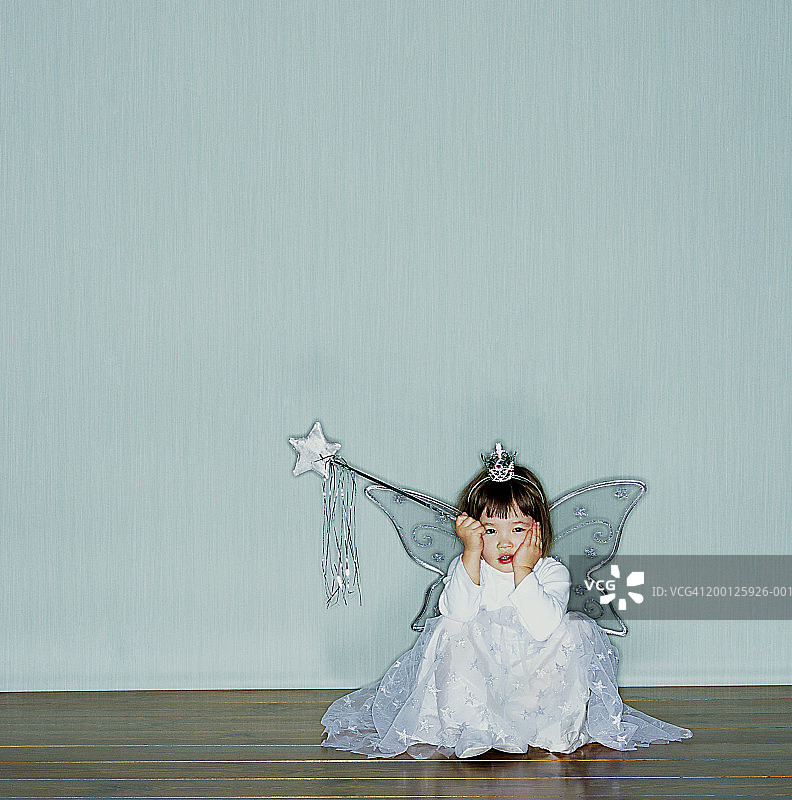 女孩(2-4)穿着天使服装坐在地板上，双手抱头图片素材