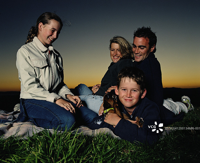 一家人坐在野餐毯上，面带微笑图片素材
