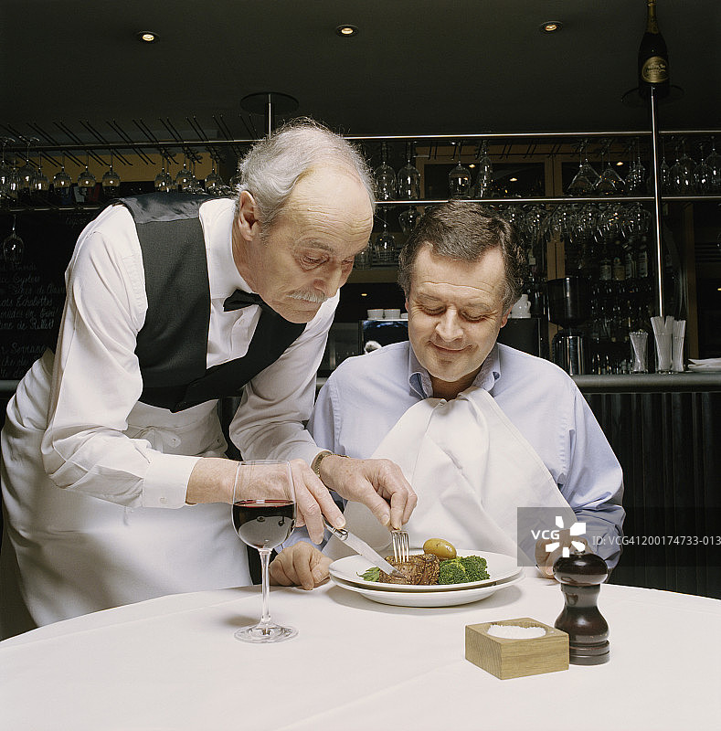 高级服务员在餐厅切盘子里的成熟男子的食物图片素材