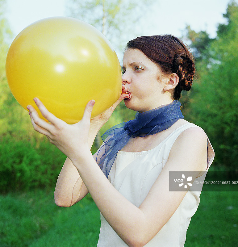 年轻女子在户外吹黄色气球图片素材