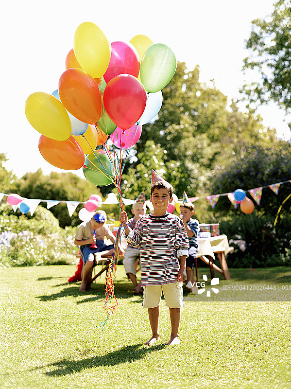 一个男孩(5-7岁)在户外拿着一堆气球，朋友在后面图片素材