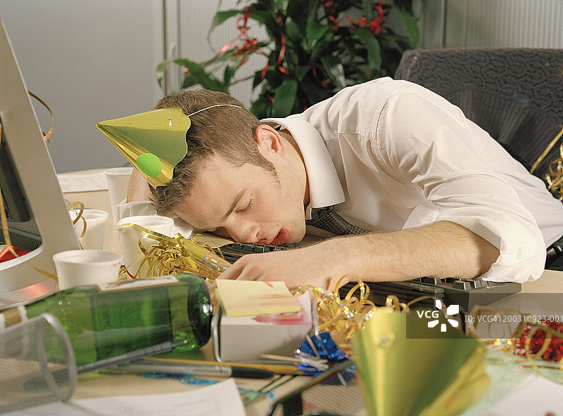 一个年轻人在桌子上睡着了，周围都是办公室派对的残留物图片素材