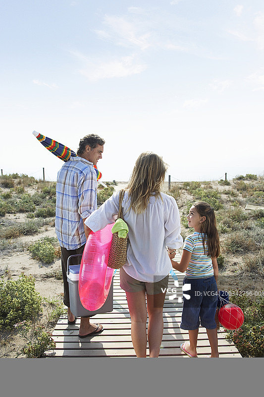 父母和女儿(6-8岁)带着野餐盒和玩具在海滩小路上图片素材