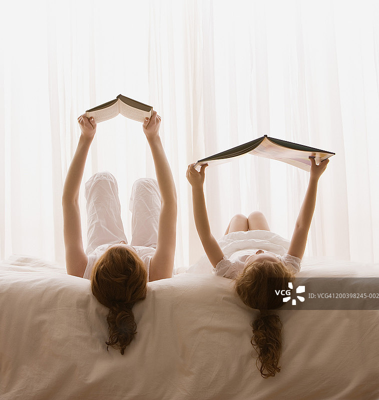 母亲和女儿(4-6)在床上看书，后视图图片素材