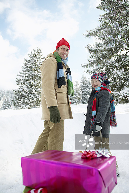 父子(8-10)在雪地里，男孩拉着雪橇，微笑着，肖像图片素材