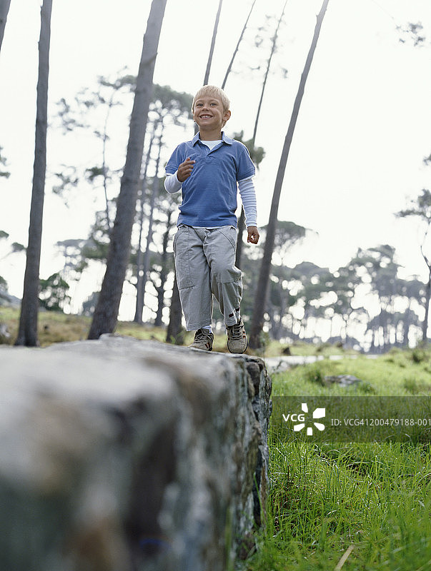 男孩(3-5)在户外的石墙上行走，面带微笑，低角度观看图片素材