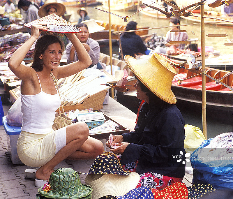 泰国，一个女人在户外的市场摊位上试帽子图片素材