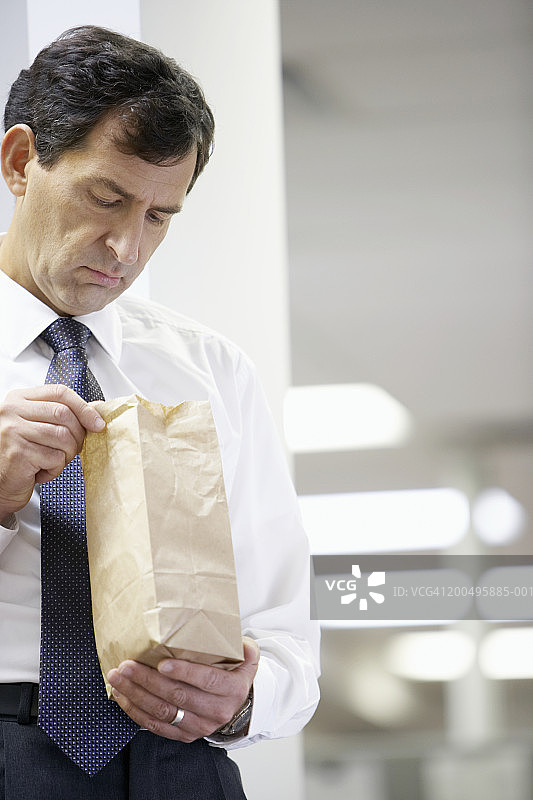 成熟的商人看着纸袋里的午餐图片素材