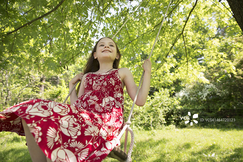 夏天。一个穿着太阳裙的女孩在秋千上挂在树枝上。图片素材