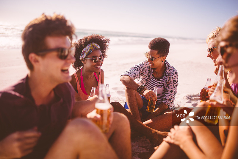 一群不同种族的朋友在海滩上喝着啤酒放松图片素材