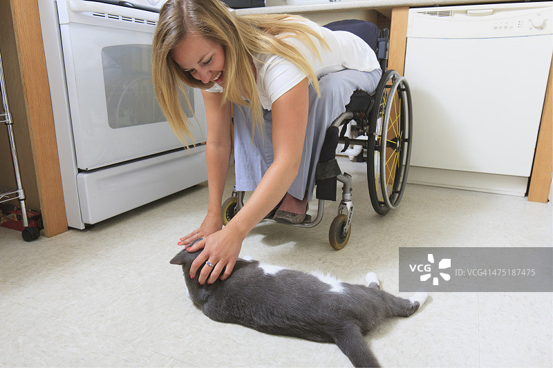 一个脊髓受伤的女人在她可接近的厨房里和她的猫玩图片素材